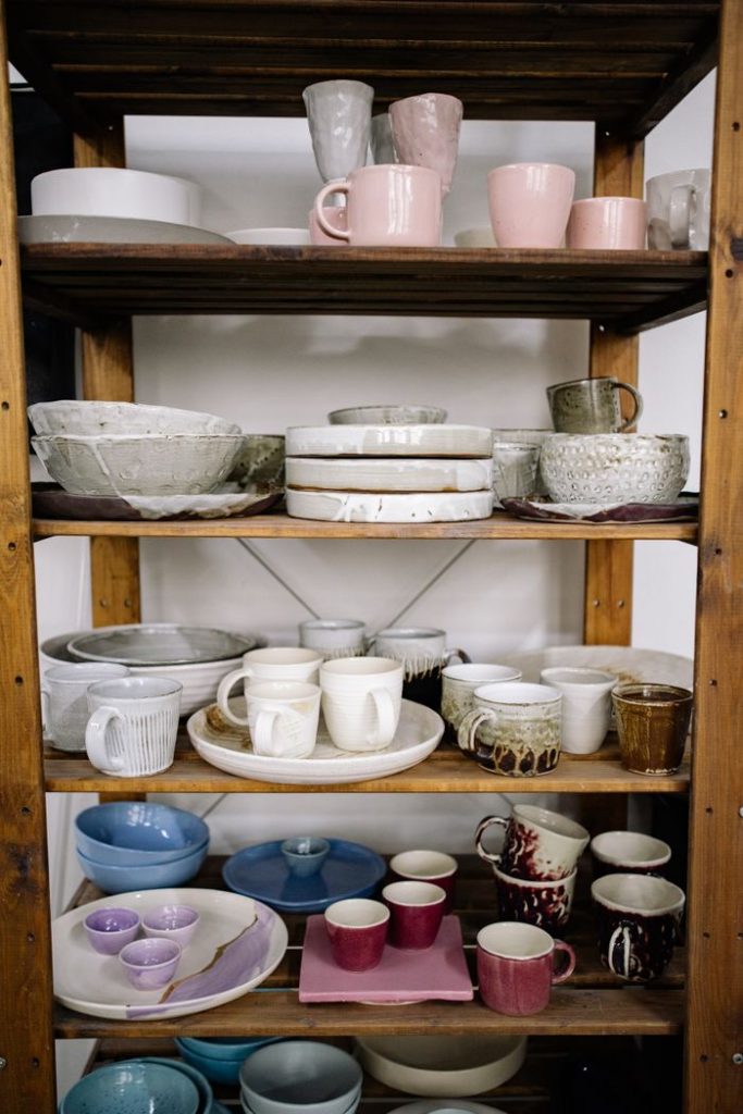 A collection of handcrafted ceramic cups and bowls displayed on wooden shelves.